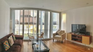 A modern living room with a sofa, a glass coffee table, a TV stand, and a balcony with large windows. - Stunningly Beautiful & Modern Apt. Small building (Miraflores)