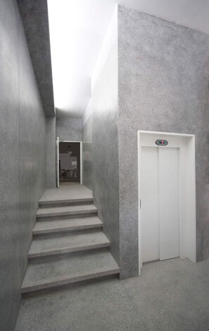 Eine schmale, betonierte Treppe führt zu einem weißen Aufzug in einem modernen Gebäude.