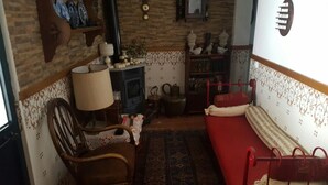 A cozy living room with a red sofa, a wooden chair, a table lamp, a fireplace, and a patterned rug. - Villa with terrace, beaches nearby as well as Évora - museum city.   (Torrao)