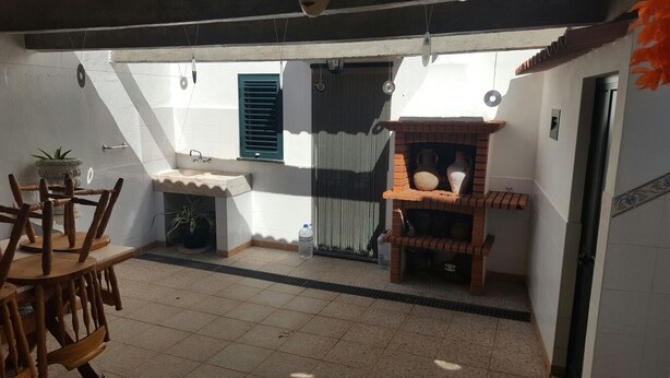 A small, enclosed patio with a tiled floor, a wooden chair, a small table, a brick shelf, a white sink, and a window with a green shutter. - Villa with terrace, beaches nearby as well as Évora - museum city.   (Torrao)