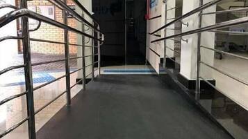 Um corredor com grades de metal, piso tátil azul e teto com iluminação linear.