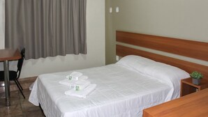 A neatly made bed with white linens and towels, a wooden headboard, a small bedside table with a plant, and a chair at a desk. - Tri Hotel Centro Chapeco (Chapecó)
