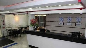 A reception area with a black reception desk, a white wall with clocks, and a small seating area with chairs and a table. - Tri Hotel Centro Chapeco (Chapecó)
