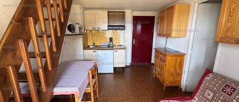 Un espacio habitable compacto con escalera de madera, kitchenette, comedor y sofá.