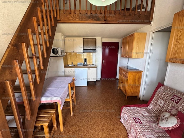 Un espace de vie compact comprenant un escalier en bois, une kitchenette, un coin repas et un canapé.