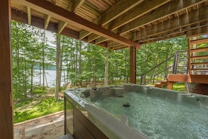 Uma banheira de hidromassagem com deck de madeira e vista para uma floresta e um lago.