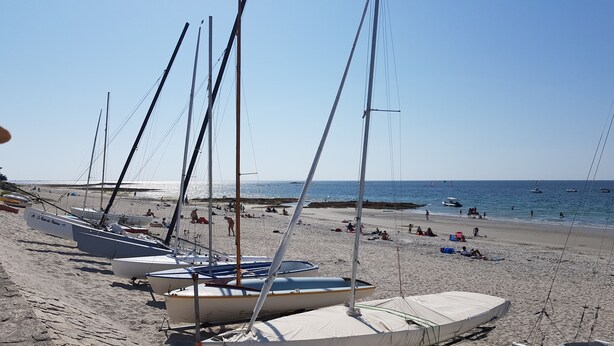 Ein Strand mit mehreren Segelbooten, die im Sand ankern, bewölkter Himmel und das Meer im Hintergrund.