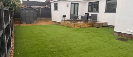 A backyard with a well-maintained lawn, a barbecue area, and a small wooden deck.