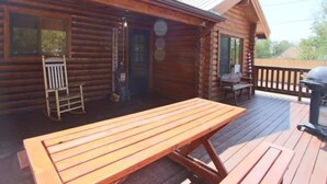 Une cabane en bois dotée d’une terrasse, d’une table de pique-nique et d’un barbecue.
