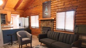 L’intérieur d’une cabane en rondins comprend un coin cuisine, une cheminée et un espace salon agrémenté d’un tapis à motifs.