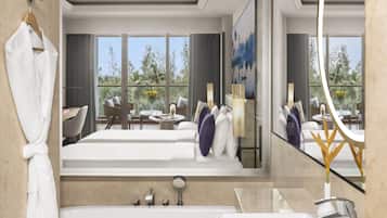 Un baño de hotel moderno con una bañera grande, una zona de ducha separada, un tocador con lavabo y un rincón de estar con mesa y sillas.