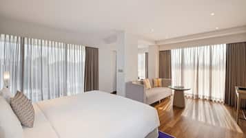 Una habitación de hotel moderna con una cama grande, un sofá, una mesita y vistas a través de cortinas translúcidas.