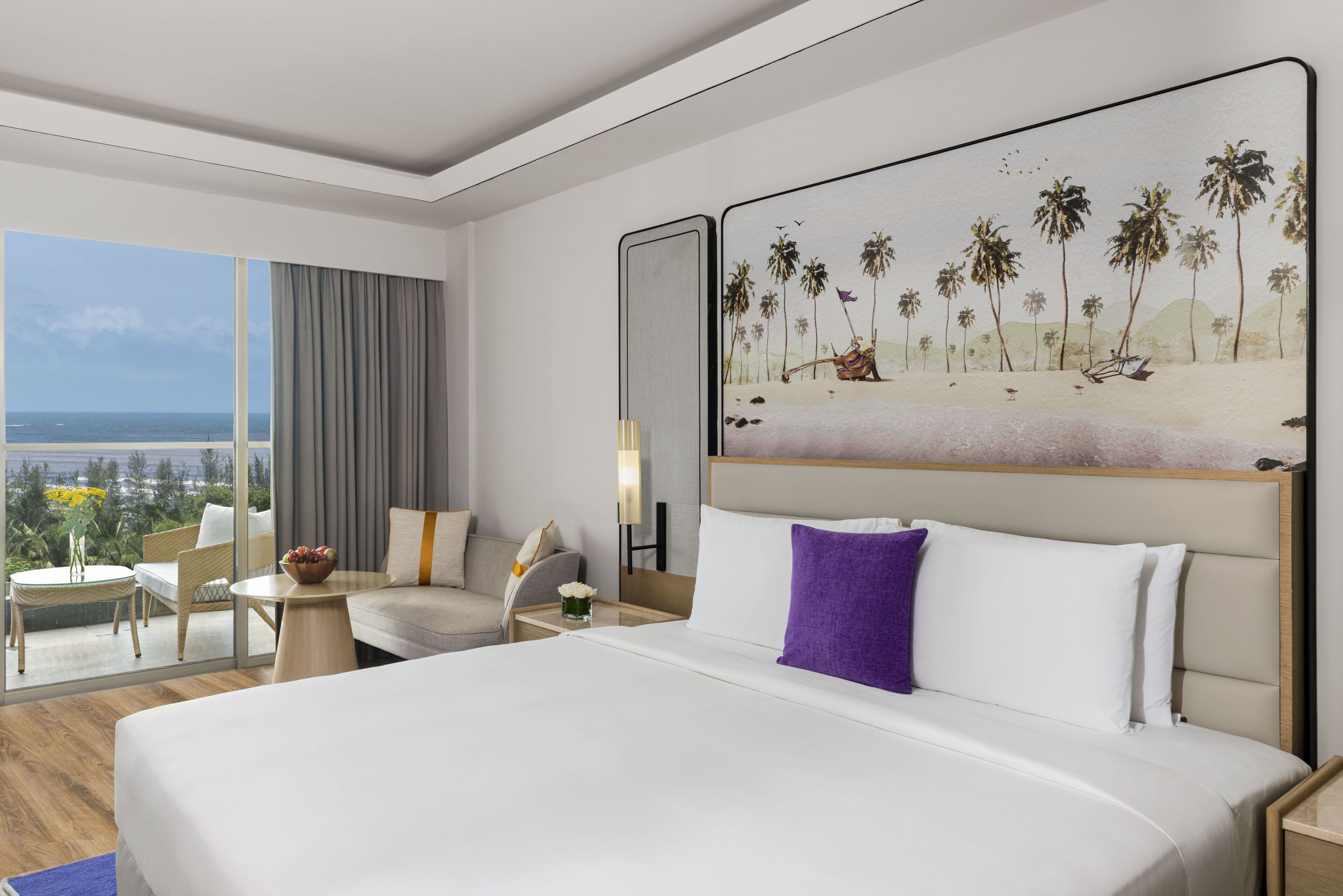 A hotel room with a large bed, a seating area with a view of the ocean, and a painting of a beach scene.