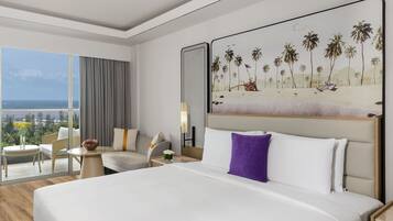 A hotel room with a large bed, a seating area with a view of the ocean, and a painting of a beach scene.