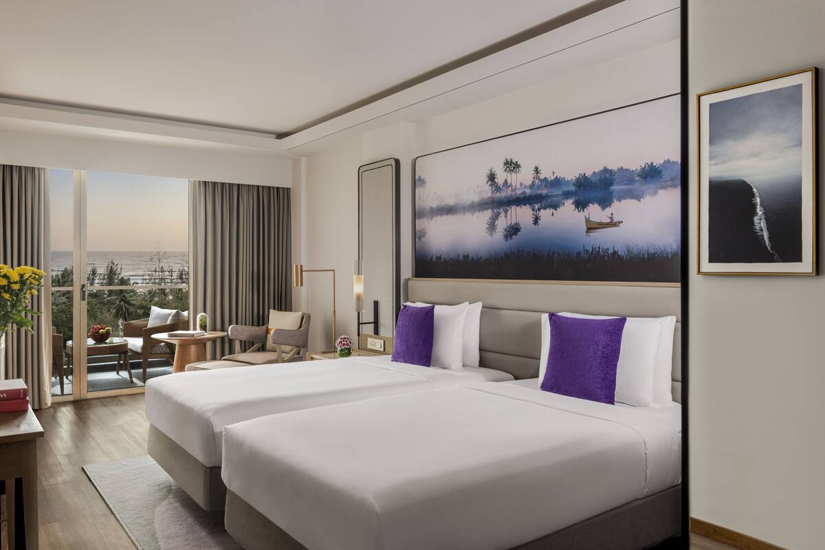 A hotel room with two beds, a balcony with a view of the sea, and a large painting of a landscape.