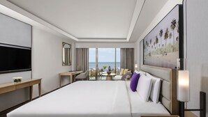 Hotelkamer met een groot bed, een bureau, een televisie en een balkon met uitzicht op zee.