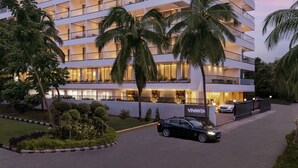 Een meerlaags hotel met balkons, een auto op de oprit, en palmbomen.