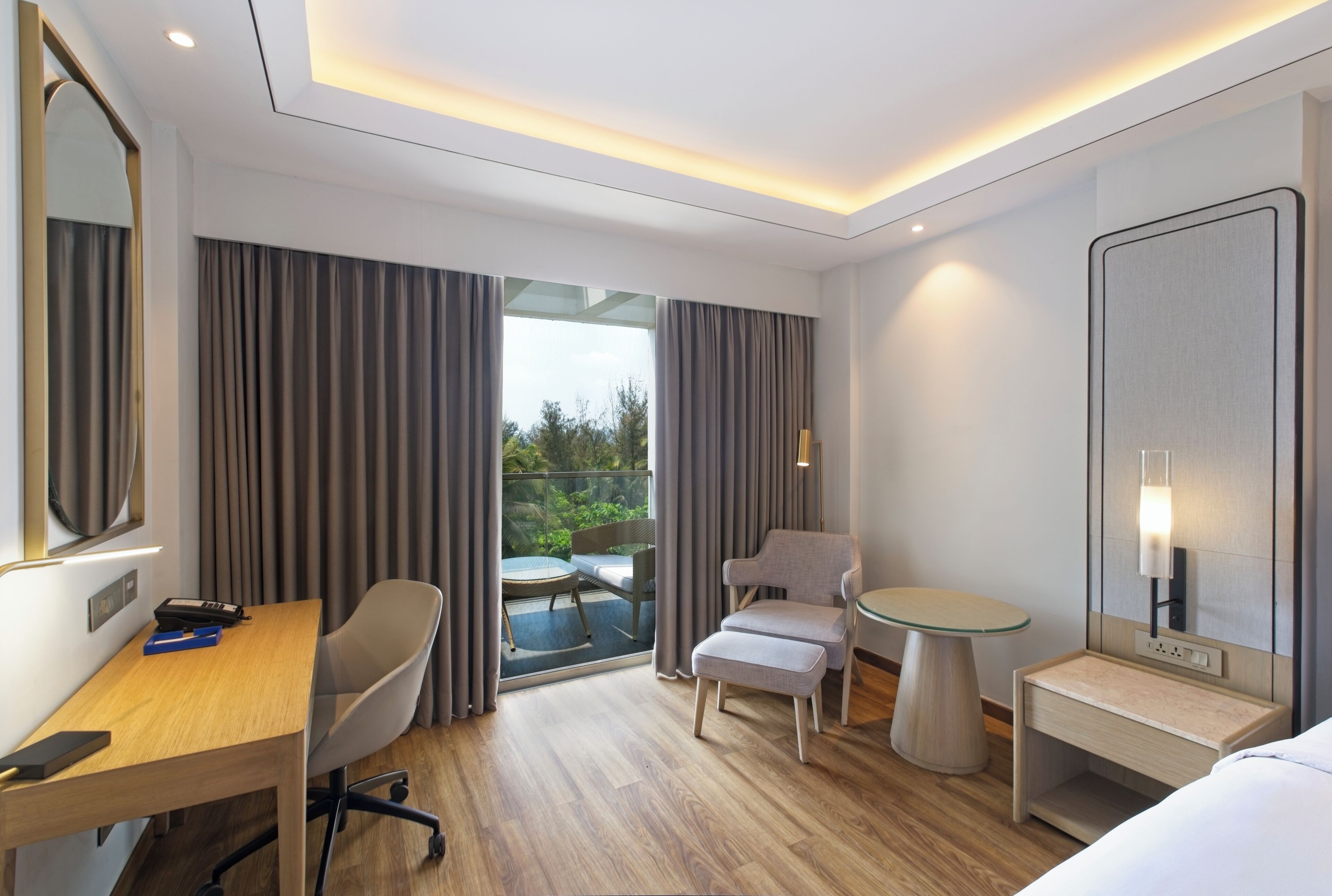 A modern hotel room with a wooden desk, a comfortable armchair, a small round table, and a bed.