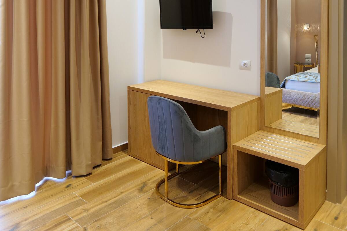 Habitación de hotel con un escritorio de madera, una silla, un televisor y un espejo grande.