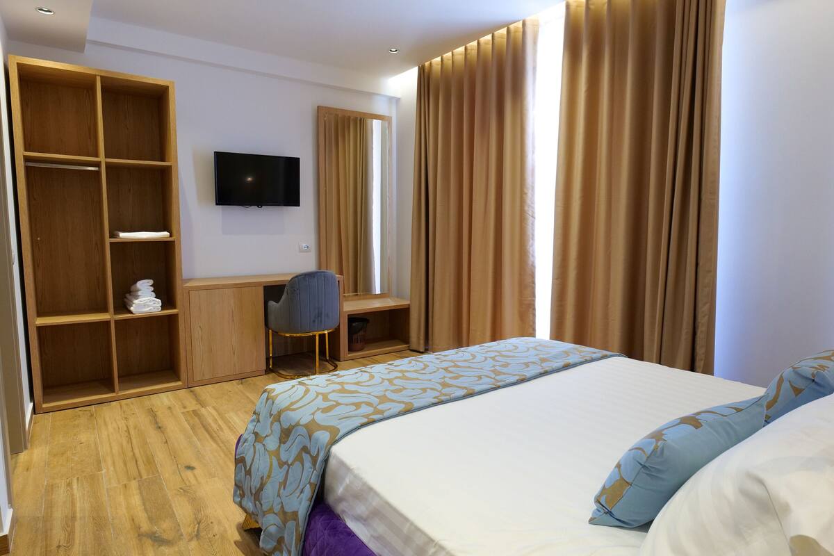 Una habitación de hotel con cama, escritorio, silla, televisor y armario.