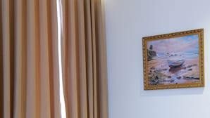 Ein Zimmer mit einem beigen Sofa, einem Strandbild und einem Fenster mit Vertikallemuren.