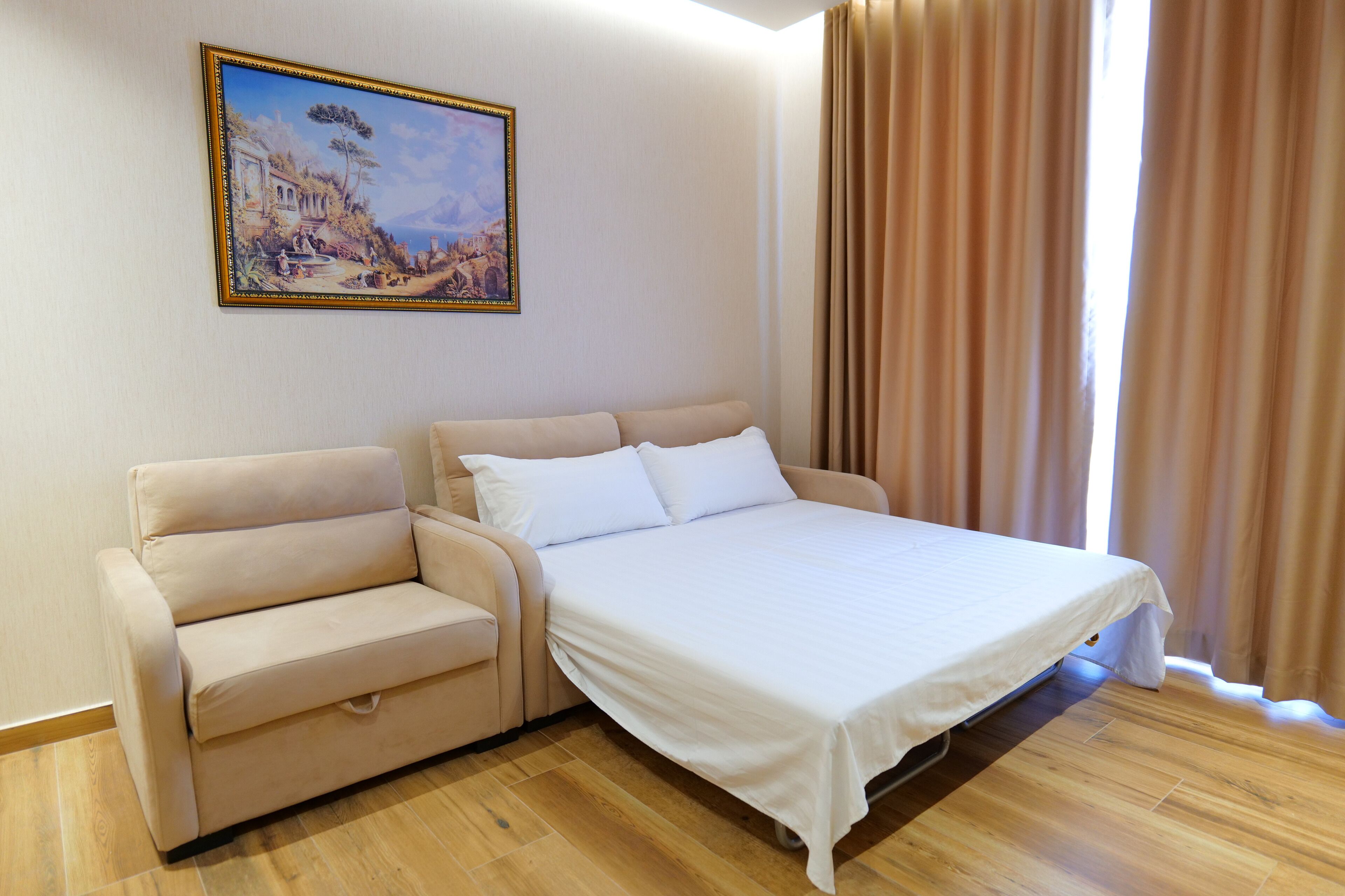 Una habitación con cama, sofá, un cuadro en la pared y una ventana con cortinas.