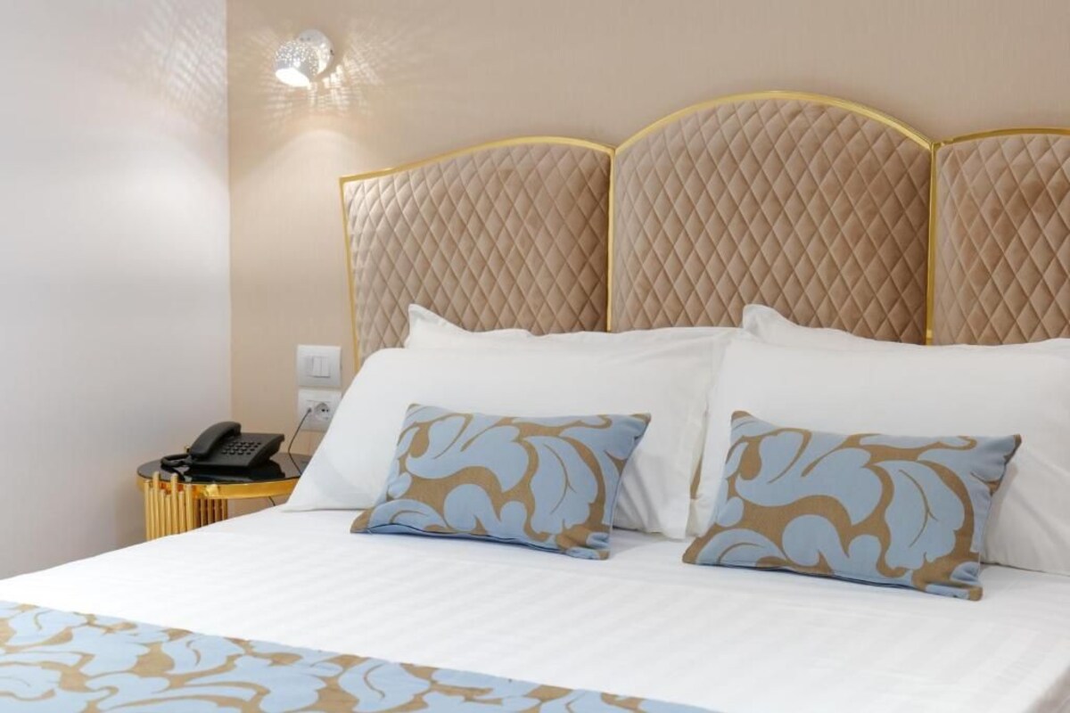 A hotel room with a large bed, a bedside table with a phone, and a wall-mounted light.