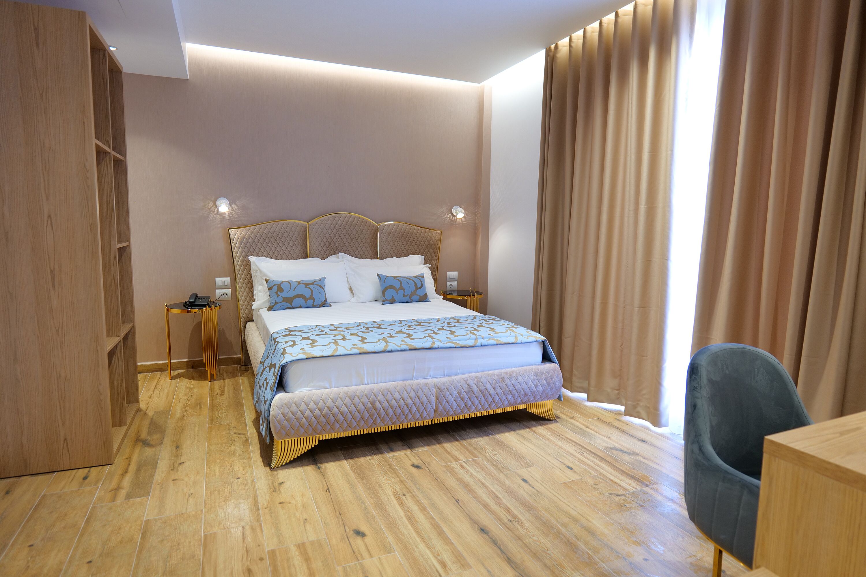 A modern bedroom with a large bed, wooden flooring, and a desk with a chair.