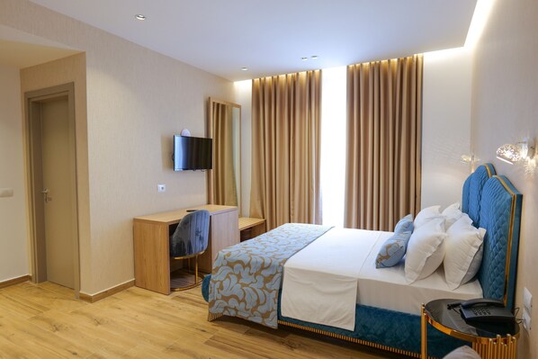 Una habitación de hotel con cama, escritorio, silla, televisor y mesita de noche con teléfono.