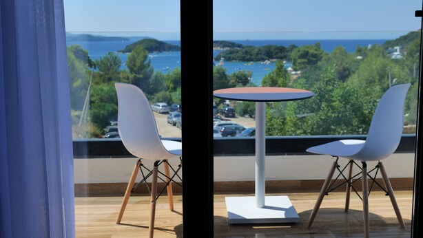 Ein Balkon mit zwei weißen Stühlen und einem runden Tisch, mit Blick auf eine malerische Wasserlandschaft und viel Grün.