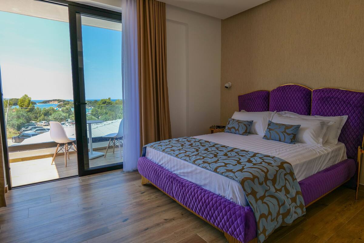 Un dormitorio con una cama grande, vistas al exterior y un balcón con una silla.