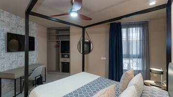 Habitación de hotel con cama, escritorio, silla, ventilador de techo y vista al exterior por una ventana.