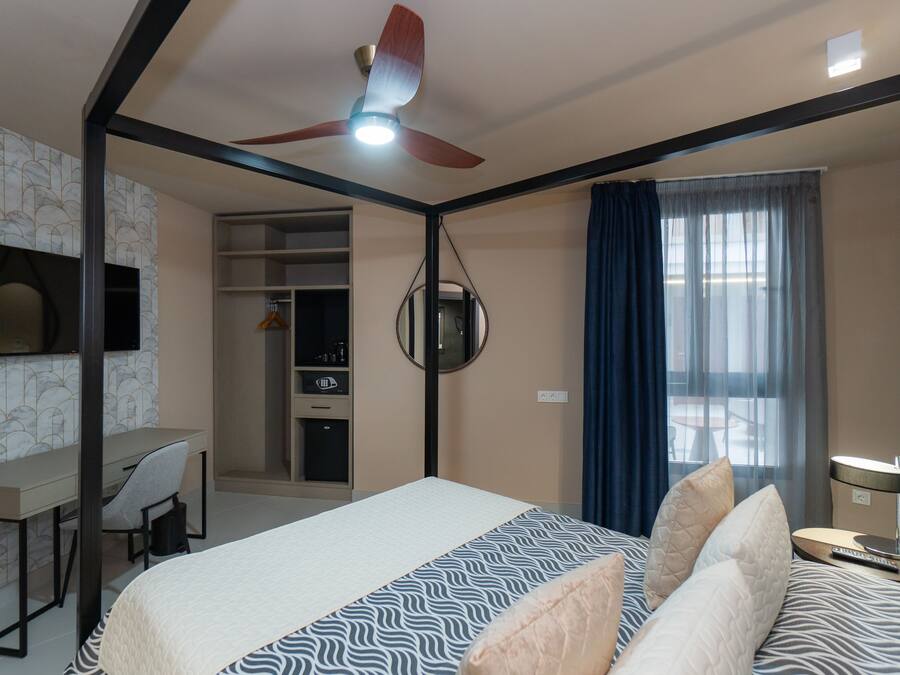 Habitación de hotel con cama, escritorio, silla, ventilador de techo y vista al exterior por una ventana.