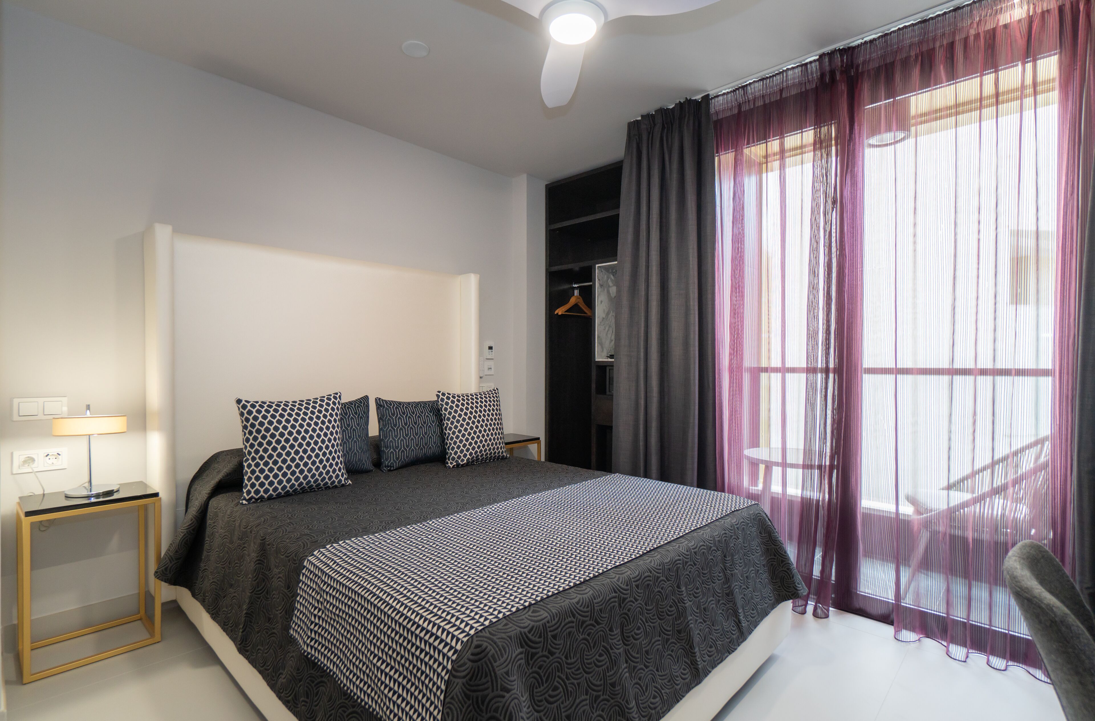 A modern bedroom with a large bed, a bedside table with a lamp, and a wardrobe.
