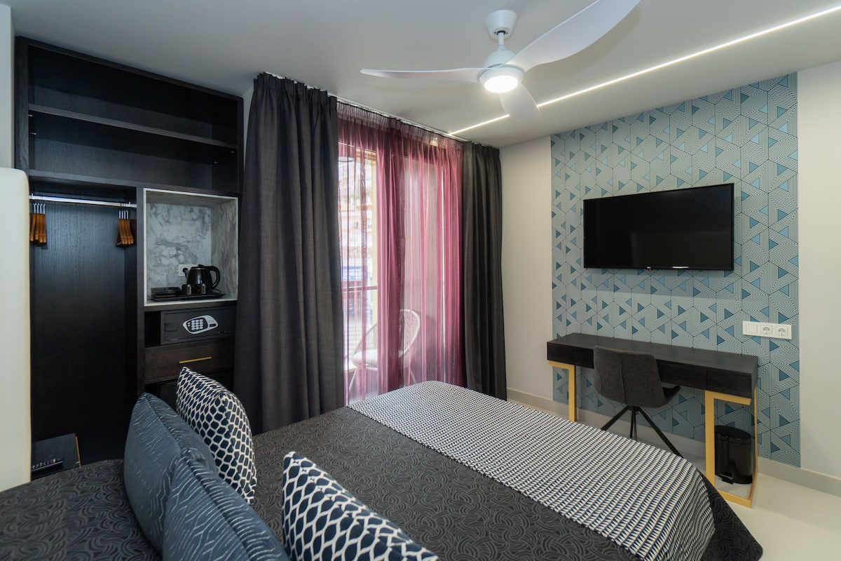 A modern bedroom with a bed, a desk, a TV, and a wardrobe.