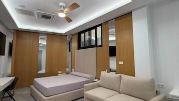 Une chambre moderne équipée d’un ventilateur de plafond, d’un éclairage encastré, d’un lit, d’un canapé et d’un bureau.
