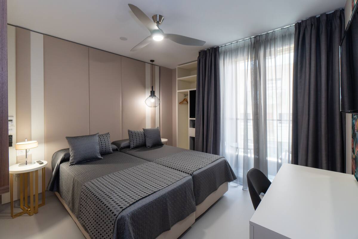 A hotel room with two beds, a desk, a ceiling fan, a lamp, and a wardrobe.