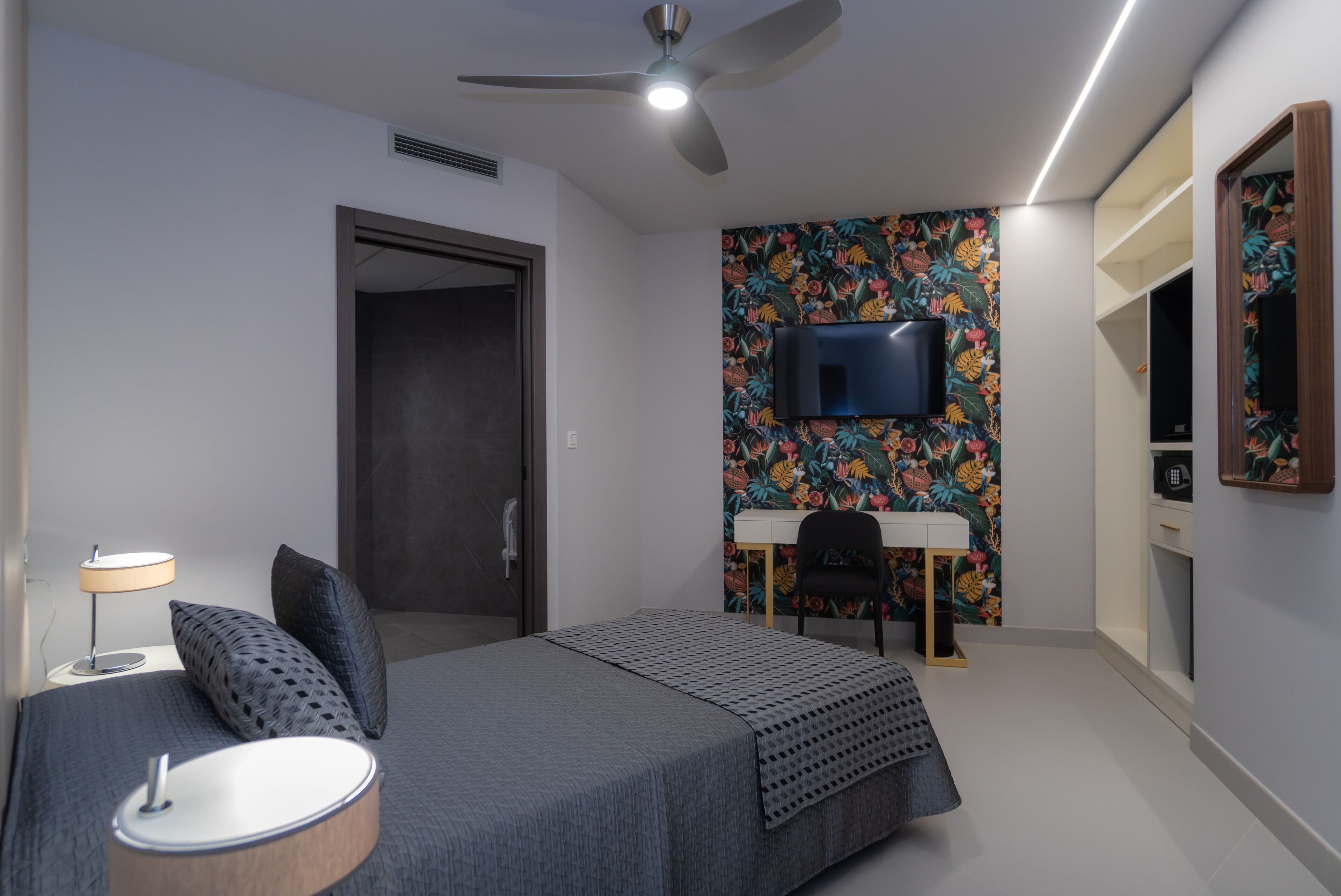 A modern bedroom with a bed, a desk, a chair, a television, and a ceiling fan.