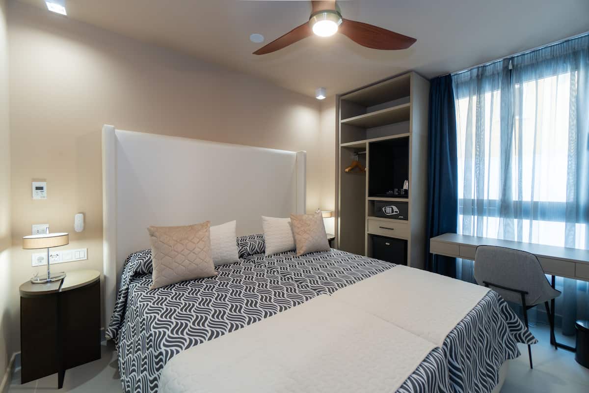 A modern hotel room with a large bed, a desk, and a wardrobe.