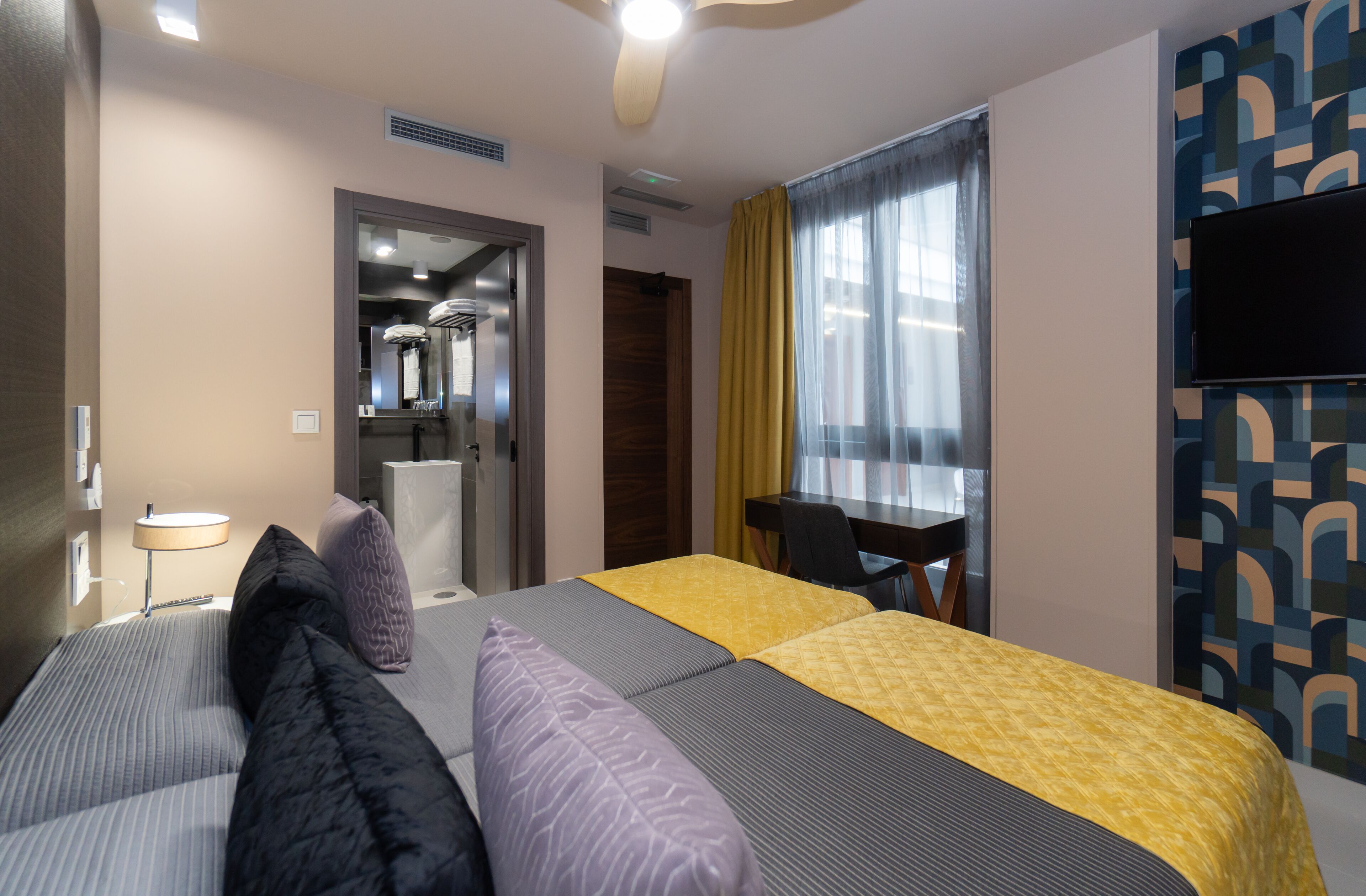 A hotel room with a bed, a desk, a television, and a bathroom visible through an open door.