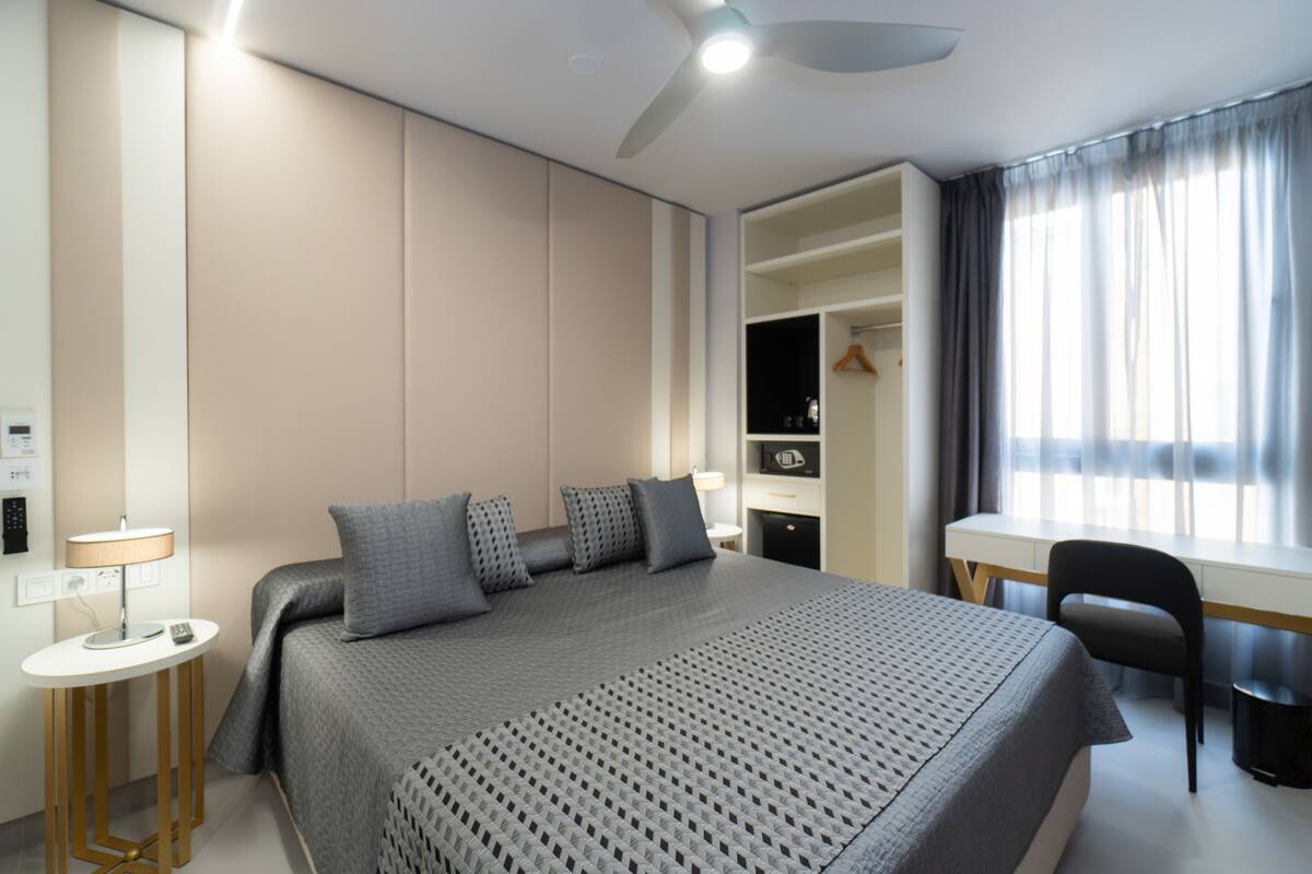 A modern hotel room with a large bed, a desk, and a wardrobe.