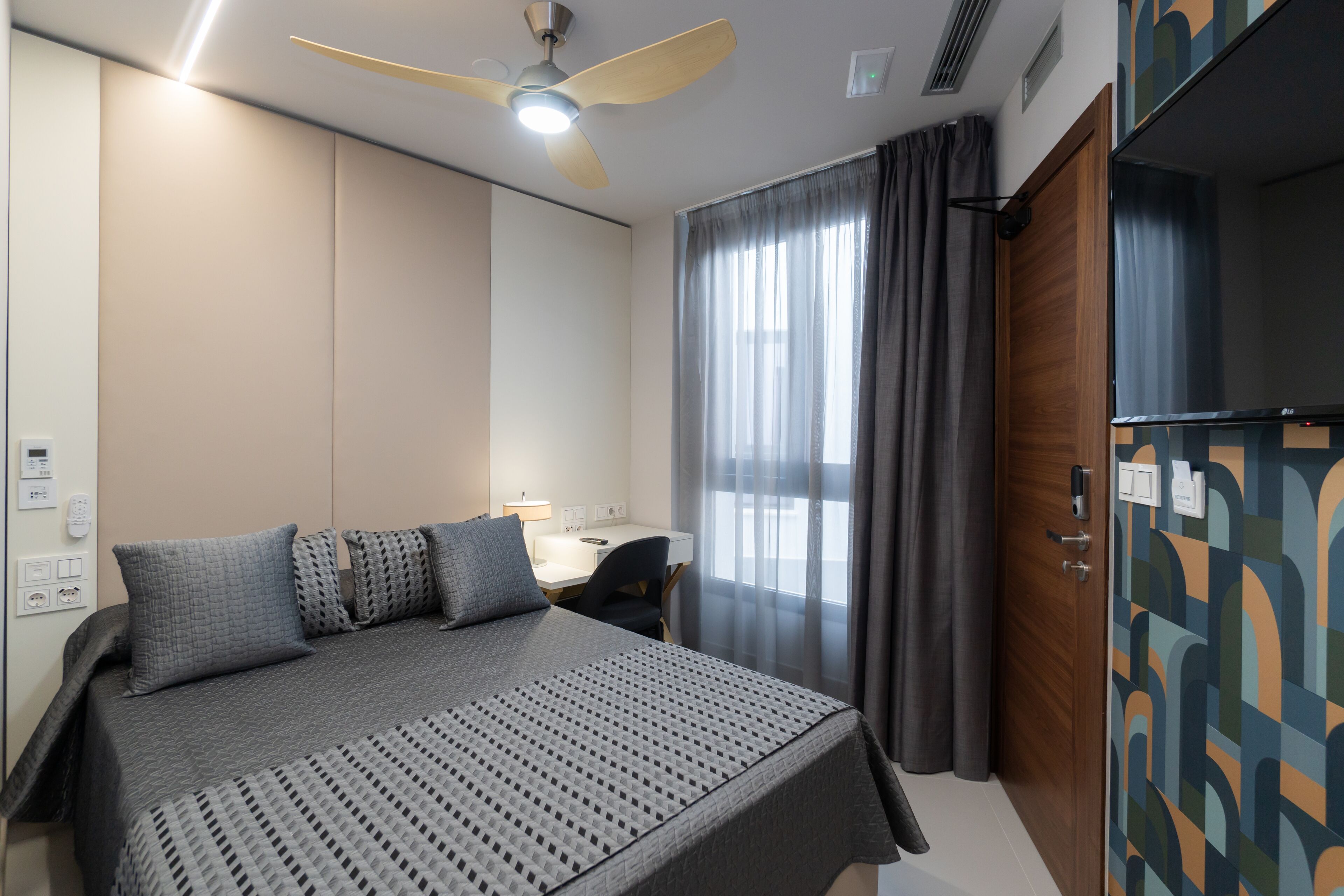 A hotel room with a bed, a desk, a chair, a ceiling fan, and a wardrobe.