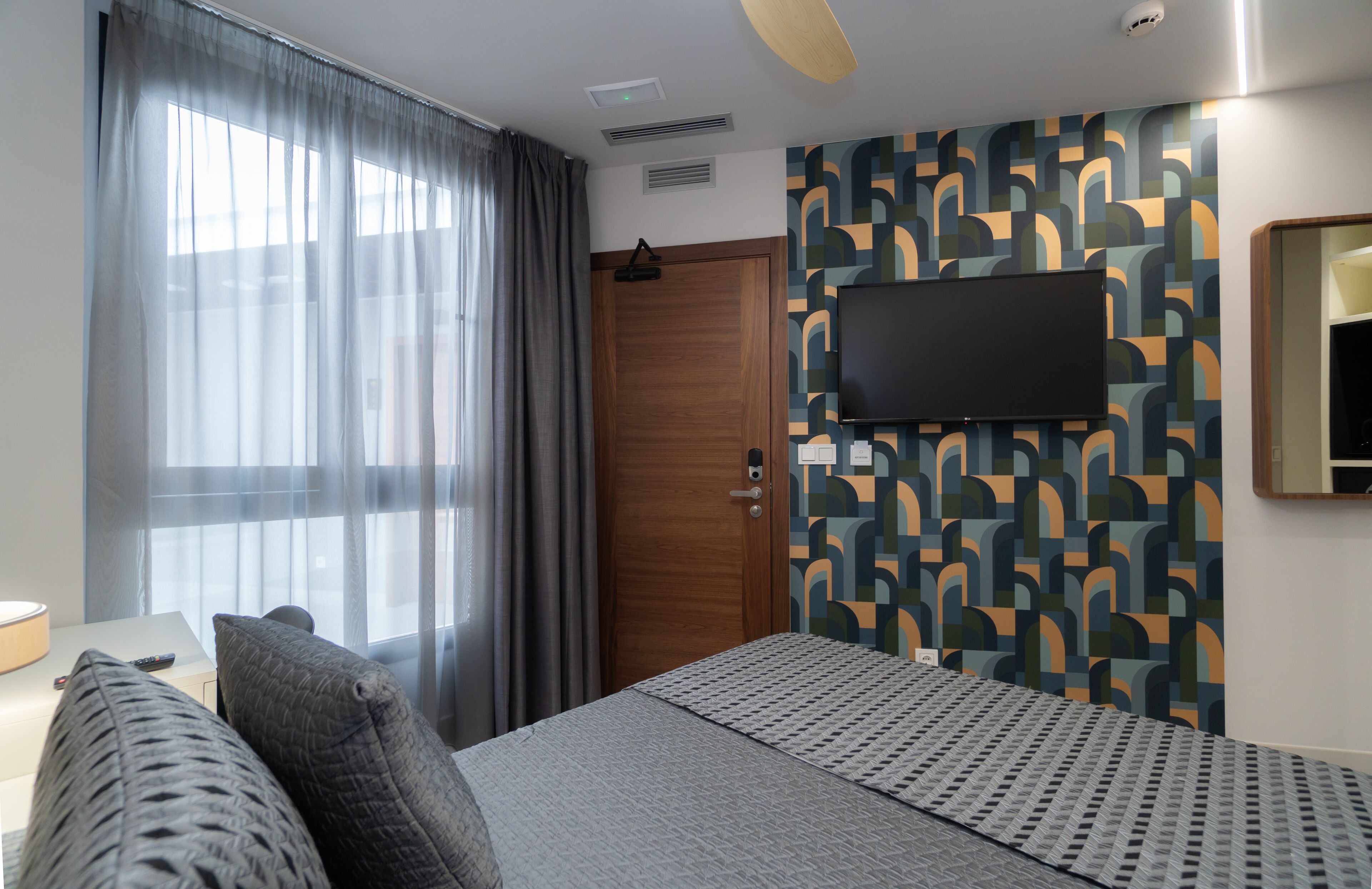 Una camera d'albergo con un letto, una TV fissata al muro, una porta in legno e una parete decorata.