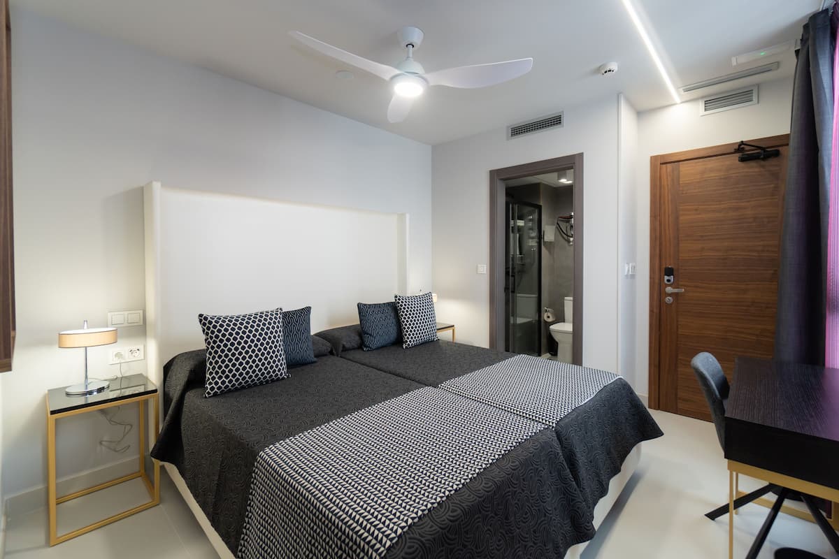 A modern bedroom with a large bed, bedside tables, a ceiling fan, and a wooden door.