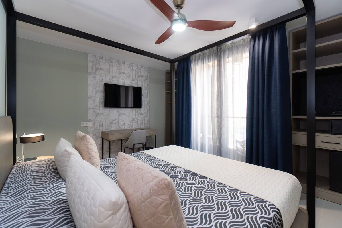 A hotel room with a bed, a desk, a chair, a TV, and a wardrobe.