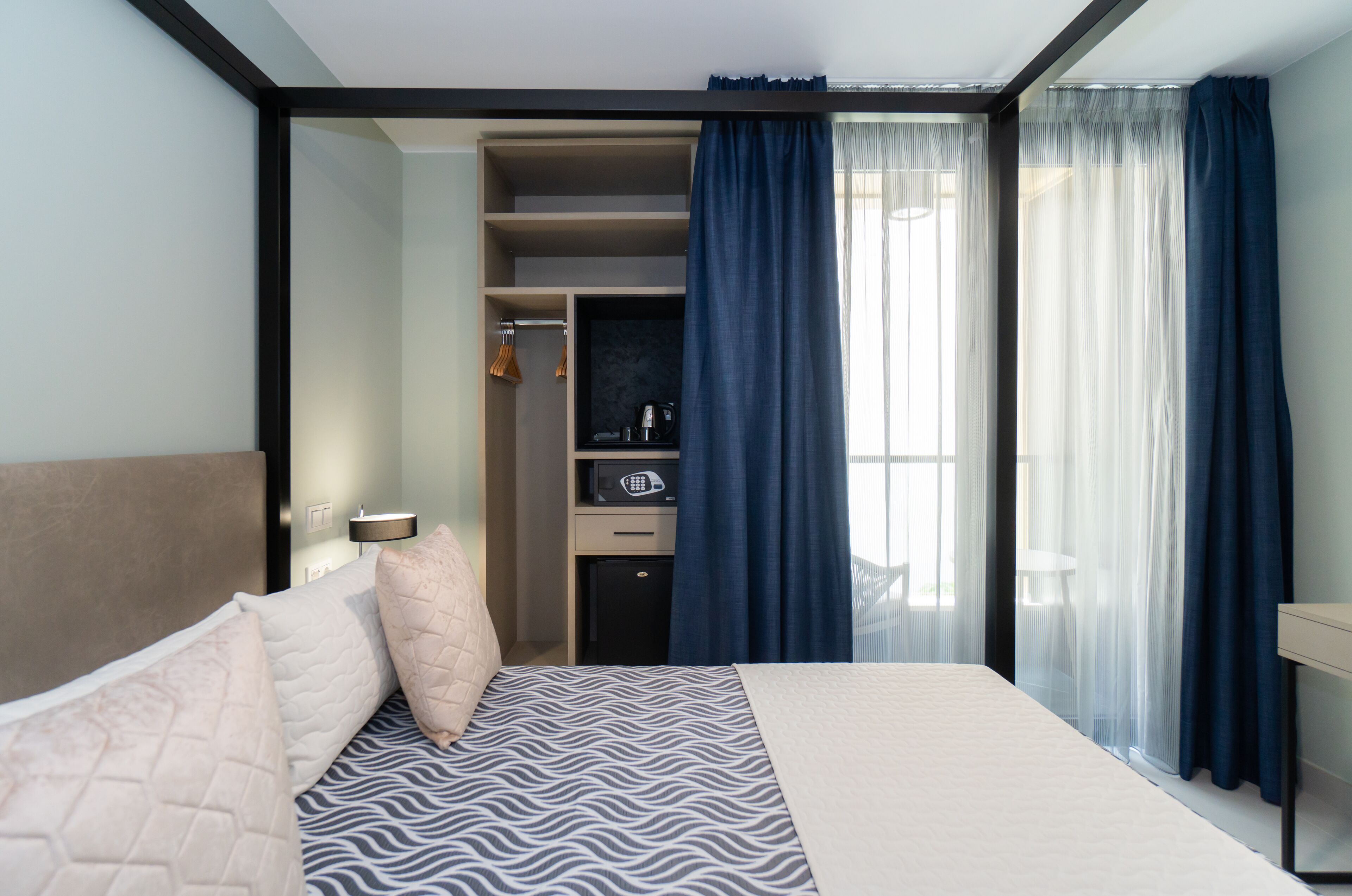 Ein modernes Hotelzimmer mit Bett, Kleiderschrank, einem kleinen Tisch und einem Schreibtisch mit Stuhl.