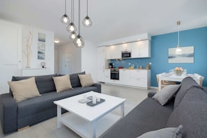 A modern living room with a grey sofa, a white coffee table, and a kitchen area with white cabinets and blue walls.