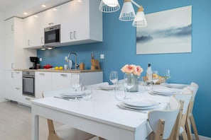 A modern kitchen with white cabinets, a microwave, and a sink. There is a dining table set with plates, glasses, and a vase of flowers.