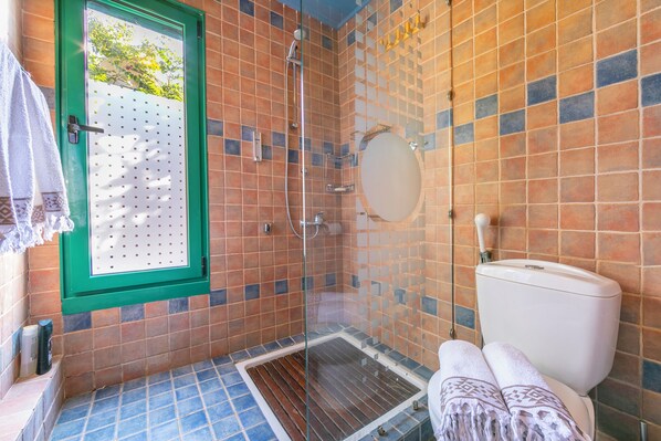 A bathroom with a shower, toilet, and a window with a view of trees.