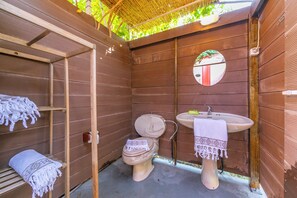 A wooden bathroom with a toilet, sink, and a shelf with towels.